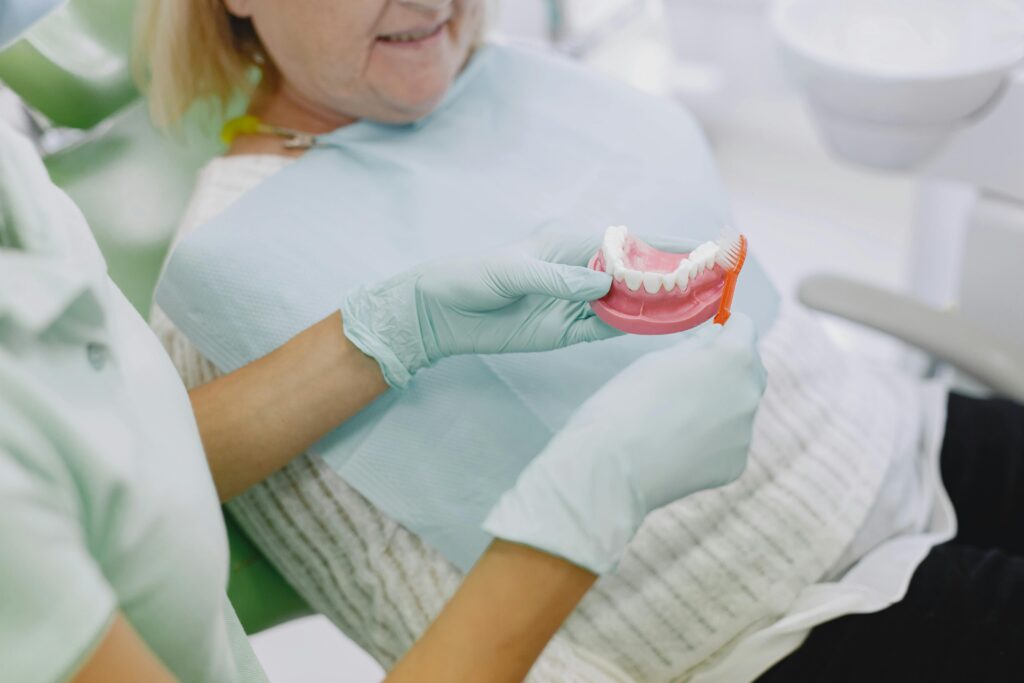 Dentures Senior woman in dental chair being shown denture brushing technique by a dental professional.